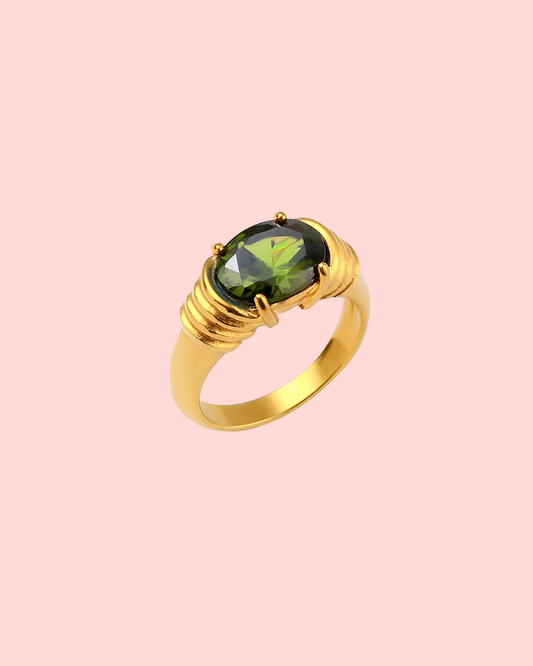 Gold ring with a green gemstone on a pink background